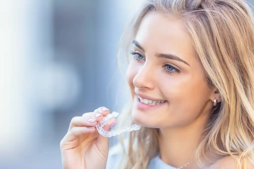 Woman holding a clear aligner before eating, demonstrating Invisalign food restrictions during daily meals